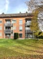 modern apartment building, red brick, large windows, multiple balconies, lawn, trees