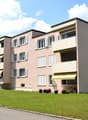 3 story apartment building, beige exterior, white windows, yellow awnings, balconies, front yard with grass and trees