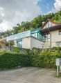 House on slope, glass balcony, terrace, brick ground floor, driveway, front and side gardens