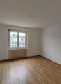 An empty room with white walls, wooden floor, a window, and a radiator.