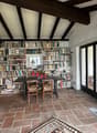 Dining room with wooden table, chairs, bookshelves, brick floor, sliding glass doors, picture frame, flowers, rug, wooden cabinet, outdoor seating