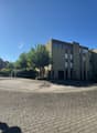 apartment building, large paved square, several trees, street lights, sunny day