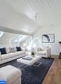 Spacious living room with vaulted ceiling, skylights, white sofa and armchair, coffee table, area rug, and a fireplace