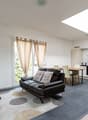 dark leather sofa, round coffee table, large rug, large white windows, white kitchen with kitchen island and breakfast table