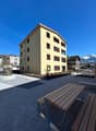 A yellow building with multiple windows, a playground, and a bench in front of it.