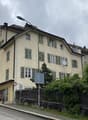 3 story building, beige exterior, multiple windows, green shutters, street light, fence, plants