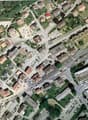 Aerial view of a town with multiple buildings, roads, and parking areas. The area is surrounded by trees and grass.
