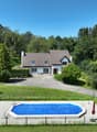 House with brown roof, white walls, 4 windows, driveway, swimming pool, green lawn, hedges, trees