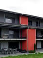 2 story house, gray and red exterior, multiple balconies, outdoor dining area, bicycles