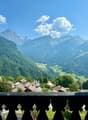 Panoramic view from a balcony with mountains, green valley, village houses, and clear blue sky