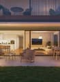 terraced apartment, glass sliding doors, outdoor seating, illuminated with warm lights, lush green landscape, wooden floors, and a clear sky