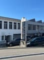 2-story commercial building with signage indicating it is a business center, several cars parked in the lot in front of the building