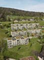 Group of residential buildings with rooftops and terraces, in a valley with trees and meadows