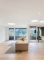 modern interior, white walls, hardwood floors, beige couch, decorative pillows, large windows with balcony, circular lights