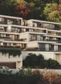 2 story apartment building, large windows, multiple balconies, multiple flower boxes, surrounded by trees, elevated location