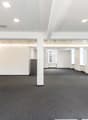 An empty office space with white walls, gray carpet, and a wooden door on the left side.