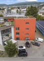 Industrial building with parking space in front, solar panels on the roof, orange facade, large glass windows