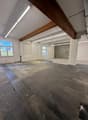 empty warehouse room with white walls, concrete floor, wooden beam ceiling, large windows, garage