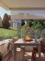 Balcony with table and chairs, glass railing, plants, view of the hills