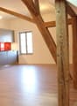attic kitchen with wooden beams, white walls, wooden floor, modern cabinets, glass window, red tiles, silver appliances