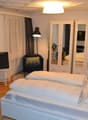 modern bedroom with double bed, white walls, wooden floor, lamps, white furniture, double doors, plants, curtains