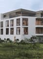Modern three-story building, white exterior, multiple balconies, glass windows, surrounded by greenery