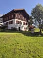 2 story house, brown and white, red shutters, large lawn, tree, mountains in the background