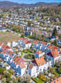 Aerial view of a residential area with many houses, some with red roofs, surrounded by trees and greenery.