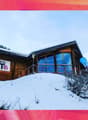 Wooden ski chalet building, big windows, covered by snow, mountain background