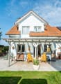 white house, red roof, solar panels, patio with wooden chairs, potted plants, wooden fence, lawn