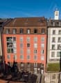 5 story building, red and white facade, many windows, balconies, green roof