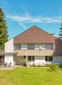 House with brown roof, white walls, large front yard, outdoor seating area, plants, trees, fence