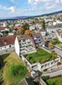 White concrete building with brown roofs, several windows, a grassy roof area, an underground garage, and multiple parking spots.