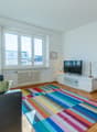 large window, white sofa, white TV unit, floor lamp, carpet, TV, plant