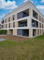 Three story apartment building, balcony on each floor, grey and beige exterior, fenced yard
