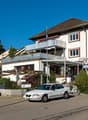 3 story building, white exterior, brown roof, balcony, parking lot, plants, flag