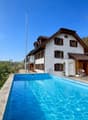 Detached house, white exterior, brown roof, large swimming pool, trees, mountains in the background