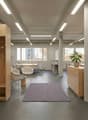 Office with modern furniture, wooden storage units, large windows, large rug, and office desks.