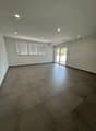 Large open living space with gray tile flooring, white walls, recessed lighting, and sliding glass doors leading to an outdoor area.