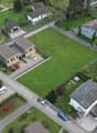 Multiple residential houses, detached garages, wide green lawns, wide roads, large open field in center