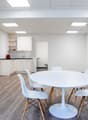 modern dining room with white round table, white chairs, light hardwood floors, modern kitchen, and built-in white cabinetry