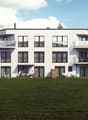 3-story modern apartment building with white exterior, large windows, and balconies. There is a grassy lawn in the foreground and parked cars visible in the background.