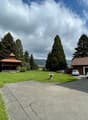 wide lawn, parked cars, detached house in the background, small wooden house, trees, mountains