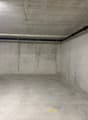 Empty parking space with concrete walls, floor, and ceiling, yellow markings, and a blue plastic bag