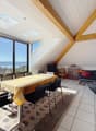 Dining area with a table and chairs, a couch, a TV, a cabinet, a rug, and large windows with a view of the sea