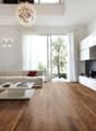 Spacious living room with hardwood flooring, large windows providing natural light, a white sectional sofa, a modern white coffee table, and a decorative chandelier overhead.