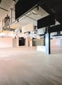 Empty room, hardwood floors, black pillars, white walls, hanging art panels, recessed ceiling lights.