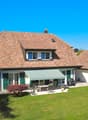 two story house, brown tile roof, balcony, green lawn, exterior patio with table and chairs, awning, window view, outdoor plants