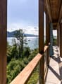 Wooden balcony with a panoramic view of a lake surrounded by mountains and trees. The balcony has large windows and a railing overlooking the scenic landscape.