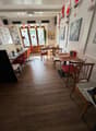 empty restaurant with wooden floor, wooden tables and chairs, white walls, decorative items, and a glass door leading to the outside